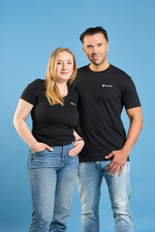 Zwei Models, Mann und Frau, beide tragen Jeanshosen und ein schwarzes T-Shirt mit weißem TRILUX Logo auf der linken Brust