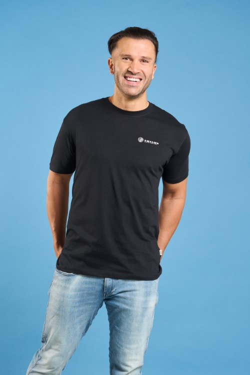 Model, lachend mit Jeans und mit schwarzem T-Shirt, mit weißem TRILUX Logo auf der Linken Brust
