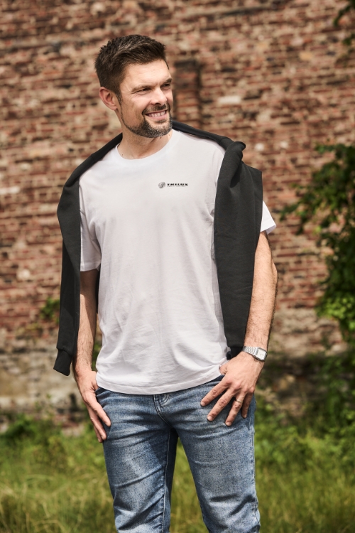 Model auf buntem Hintergrund, Trägt Jeanshose, schwarzen Pulli über den Schultern, weißes T-Shirt mit TRILUX Logo auf der linken Brust