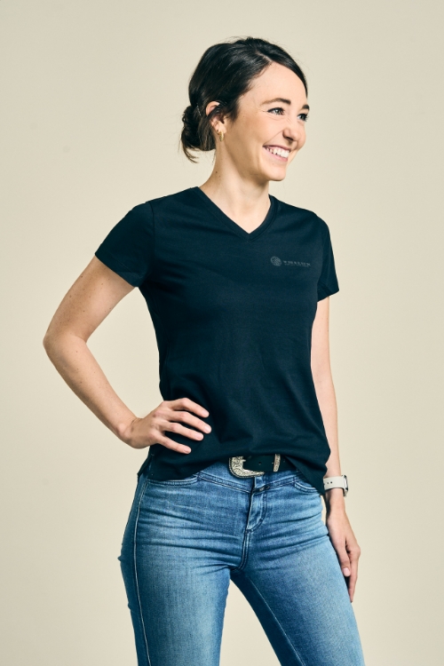 Weibliches Model trägt eine Jeanshose und ein schwarzes T-Shirt mit V-Ausschnitt, weißes TRILUX Logo auf der linken Brust
