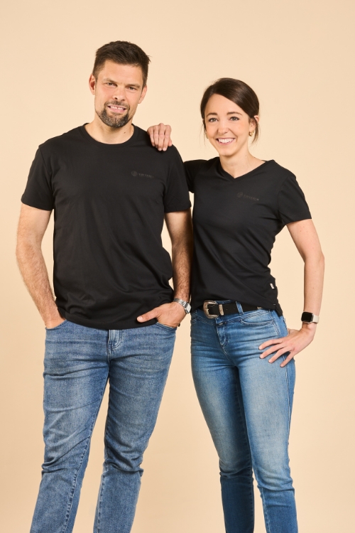 Zwei Models, Mann und Frau Posen in Jeanshosen, tragen schwarze T-Shirts mit weißem TRILUX Logo auf der linken Brust