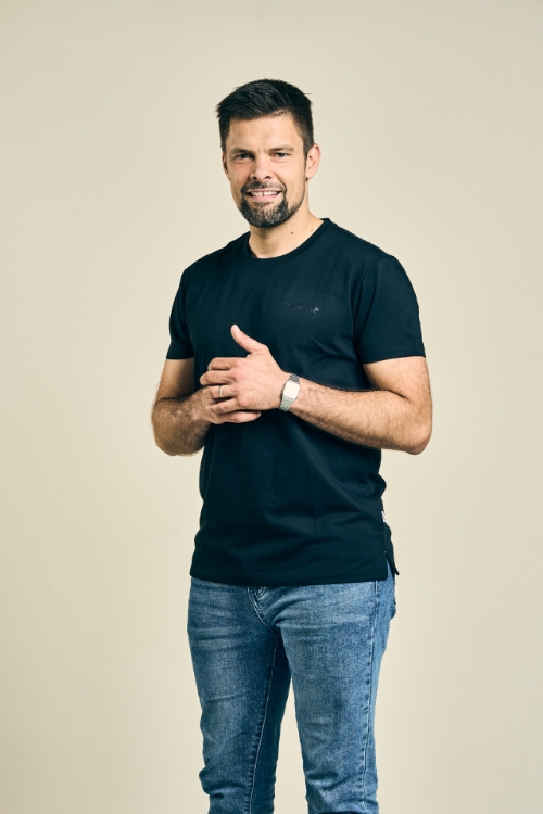 Männliches Model trägt Jeanshose und schwarzes T-Shirt mit weißem TRILUX Logo auf linker Brust