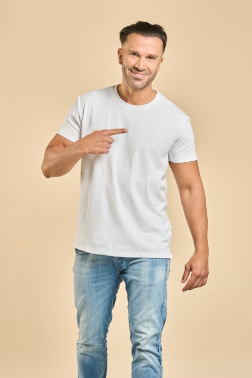 Männliches Model trägt weißes T-Shirt und zeigt mit Finger auf weißes TRILUX Logo auf der linken Brust