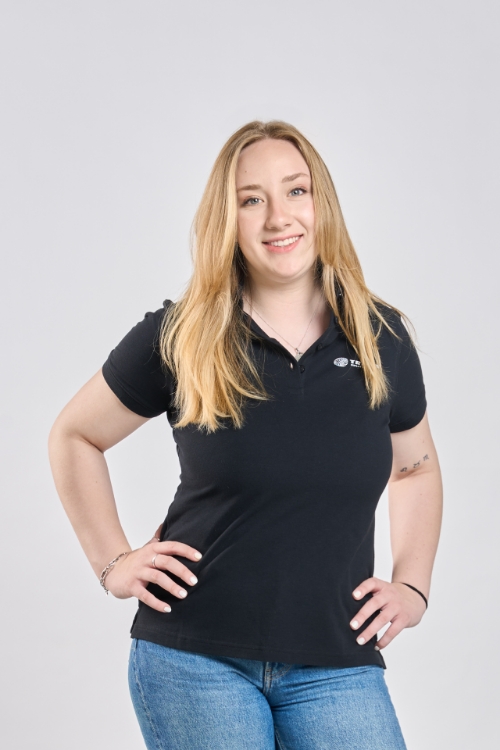 Weibliches Model trägt Jeasnhose und Schwarzes Poloshirt mit drei Knöpfen, weißes TRILUX Logo auf linker Brust