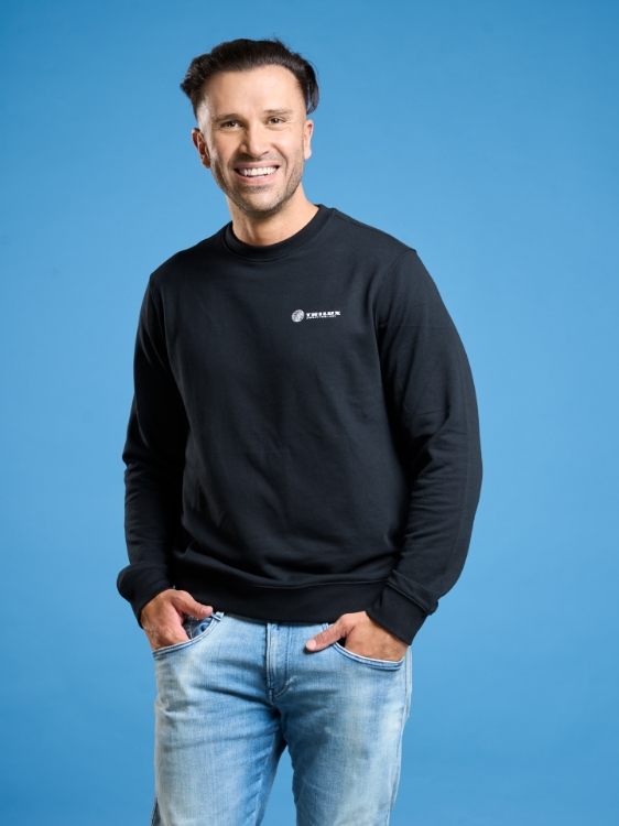 Männliches Model trägt Jeanshose und Schwarzes Sweatshirt mit weißem TRILUX Logo auf der Linken Brust