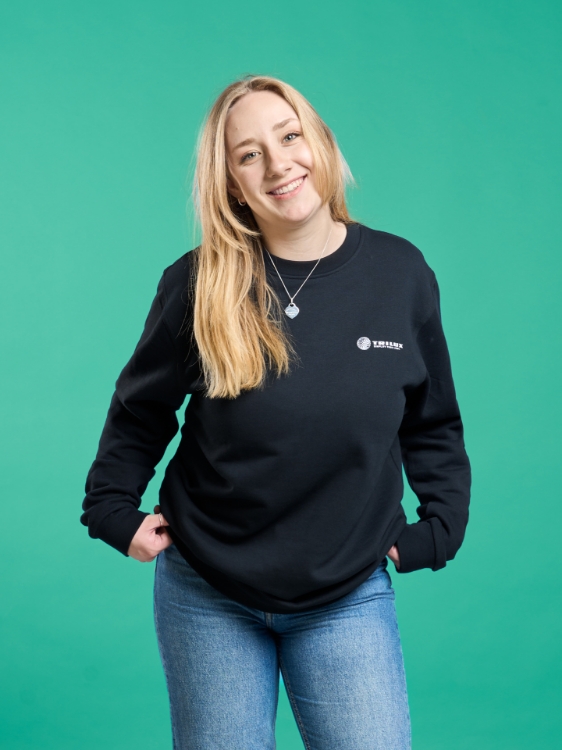 Weibliches Model trägt Jeanshose und Schwarzes Sweatshirt mit weißem TRILUX Logo auf der Linken Brust