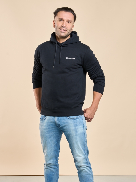 Männliches Model trägt Jeanshose und Schwarzes Kapuzensweatshirt mit weißem TRILUX Logo auf der linken Brust