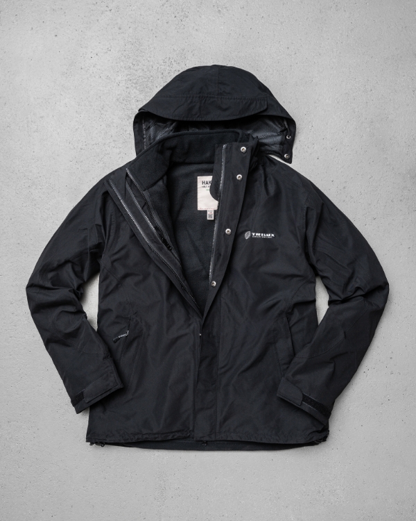 Schwarze Jacke mit Kapuze, weißes TRILUX Logo auf der linken Brust